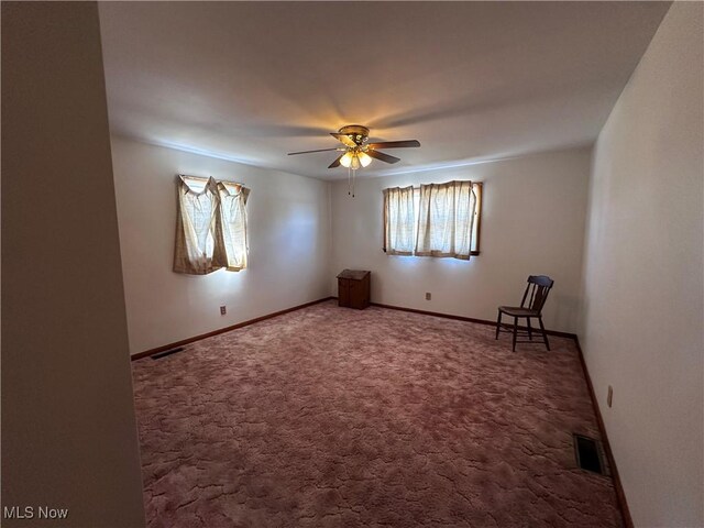 carpeted spare room featuring baseboards, visible vents, and ceiling fan