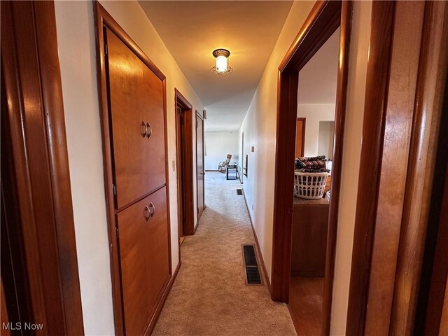 hall with baseboards, visible vents, and light carpet