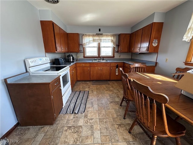 kitchen featuring a sink, electric range, brown cabinetry, and stone finish flooring