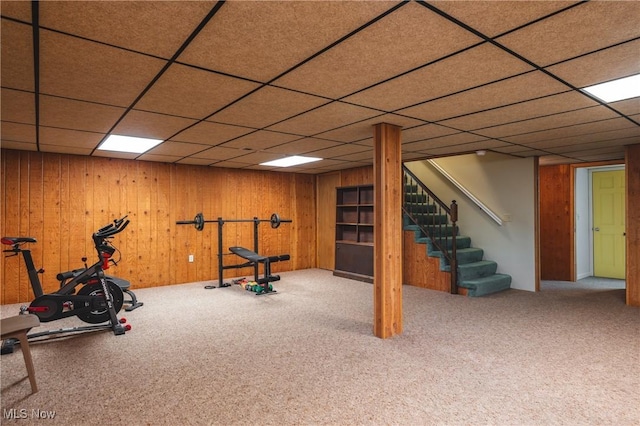 exercise room featuring wooden walls, carpet, and a drop ceiling