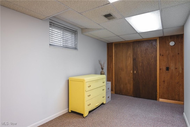 carpeted bedroom with visible vents, baseboards, a drop ceiling, wood walls, and a closet