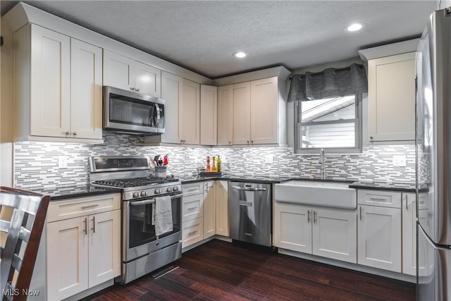 kitchen with dark wood-type flooring, a sink, dark countertops, tasteful backsplash, and stainless steel appliances