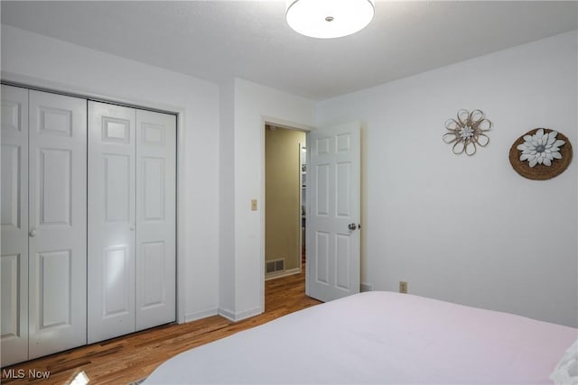 bedroom featuring wood finished floors, visible vents, and a closet