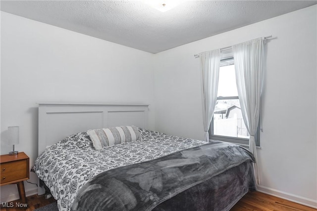 bedroom featuring multiple windows, wood finished floors, baseboards, and a textured ceiling