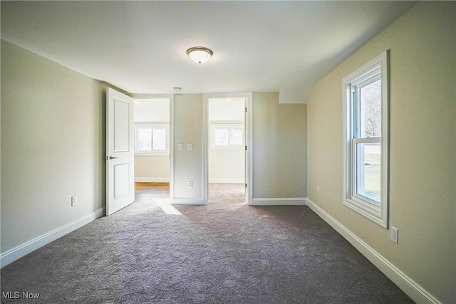 spare room featuring baseboards and dark colored carpet