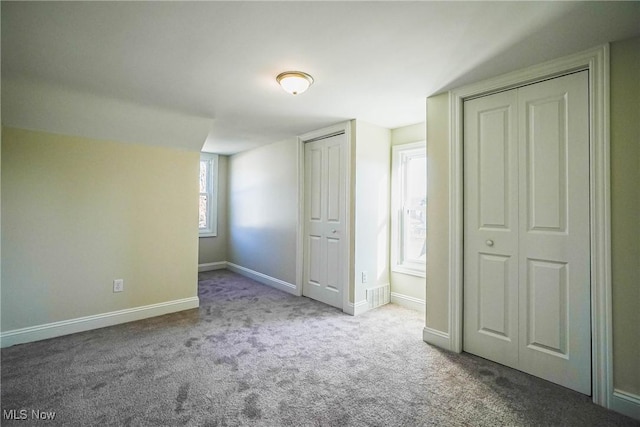 unfurnished bedroom with visible vents, baseboards, carpet, and multiple closets