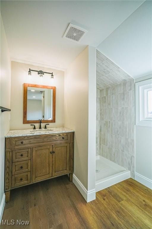 bathroom featuring visible vents, wood finished floors, a tile shower, baseboards, and vanity