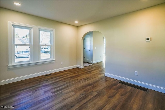 unfurnished room with dark wood-style floors, visible vents, baseboards, recessed lighting, and arched walkways