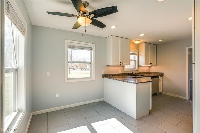 kitchen featuring stainless steel dishwasher, a peninsula, light tile patterned flooring, and a sink