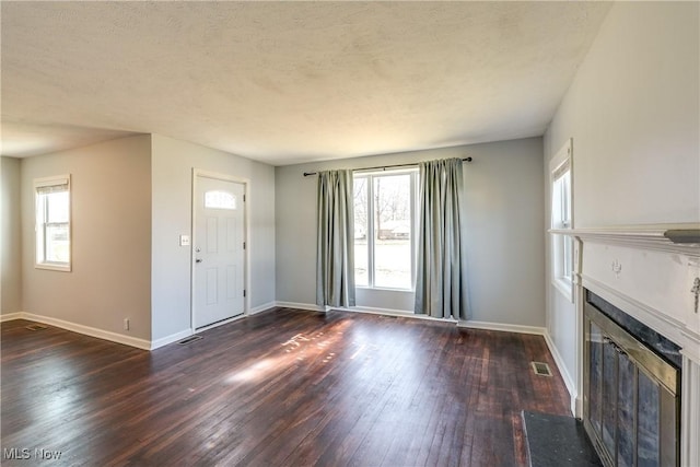 unfurnished living room with a glass covered fireplace, plenty of natural light, visible vents, and dark wood-style flooring