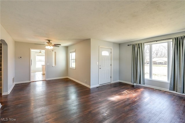 interior space featuring dark wood-style floors, arched walkways, a wealth of natural light, and baseboards