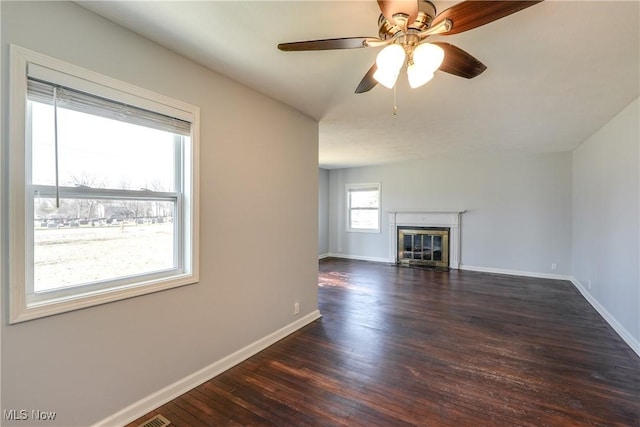 unfurnished living room with dark wood-style floors, a glass covered fireplace, ceiling fan, and baseboards