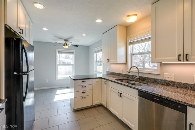 kitchen with a sink, dark stone countertops, stainless steel dishwasher, freestanding refrigerator, and a peninsula