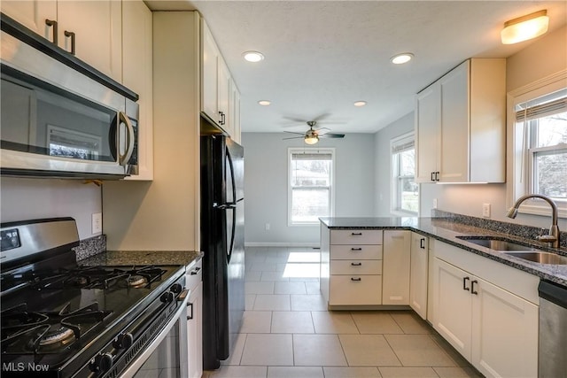 kitchen with a sink, stainless steel appliances, dark stone counters, a peninsula, and white cabinets