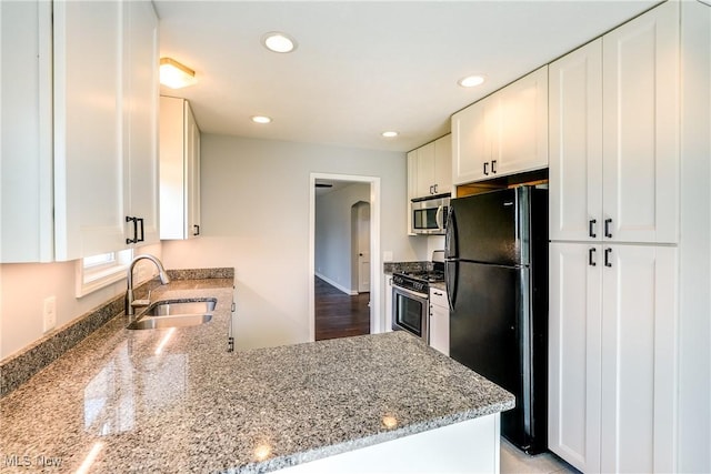 kitchen with a sink, light stone counters, stainless steel appliances, arched walkways, and white cabinets