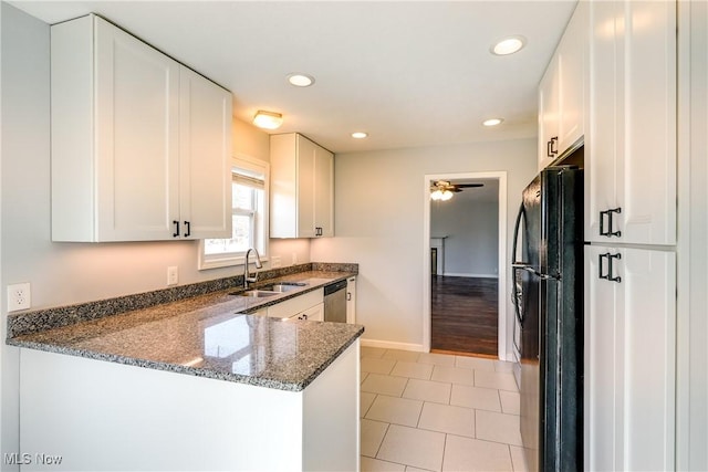 kitchen featuring a sink, dark stone counters, white cabinetry, and freestanding refrigerator