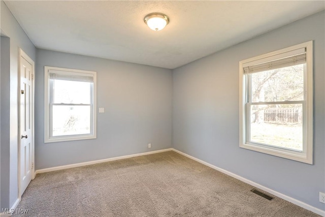 unfurnished room with carpet flooring, a healthy amount of sunlight, visible vents, and baseboards