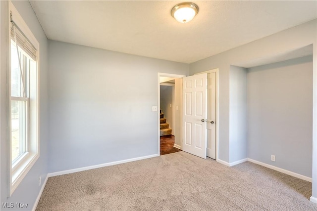 spare room featuring baseboards, carpet floors, and stairway