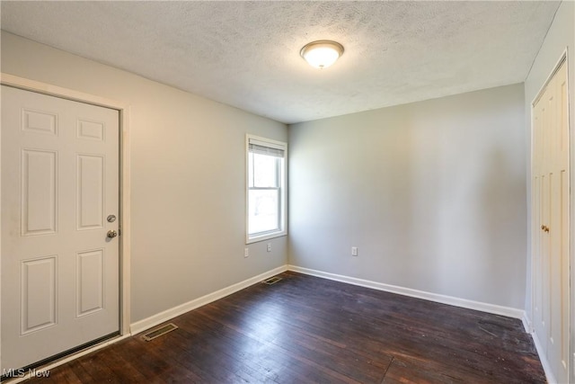 spare room featuring dark wood-type flooring, baseboards, visible vents, and a textured ceiling