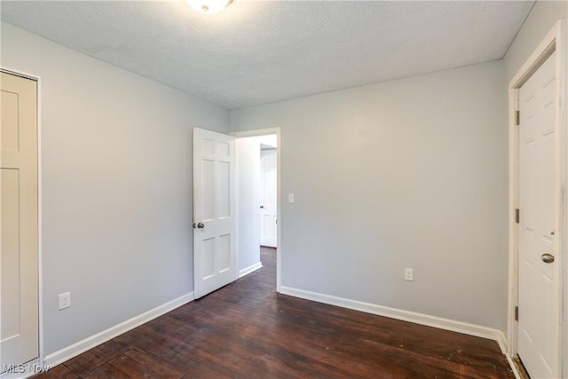 unfurnished bedroom with dark wood-style floors, a textured ceiling, and baseboards