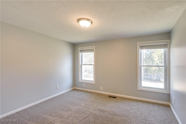 carpeted spare room featuring visible vents, a textured ceiling, and baseboards