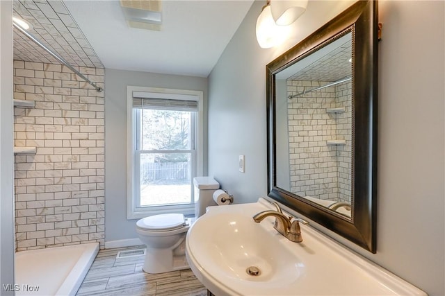 bathroom featuring a sink, visible vents, tiled shower, and toilet