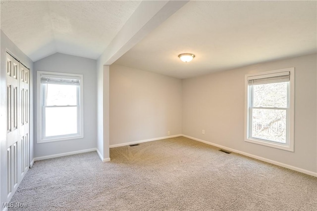 carpeted spare room featuring visible vents, a textured ceiling, baseboards, and vaulted ceiling