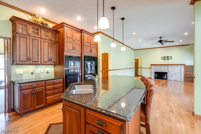 kitchen with a sink, black appliances, a center island with sink, and light wood finished floors