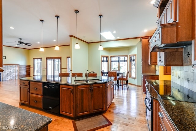 kitchen with light wood finished floors, a kitchen island with sink, a sink, decorative backsplash, and black appliances