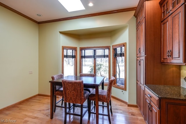 dining area with baseboards, light wood-style floors, a skylight, and crown molding