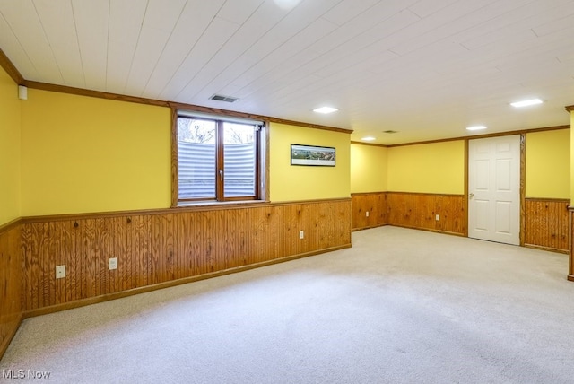 unfurnished room featuring visible vents, ornamental molding, wood walls, carpet flooring, and wainscoting