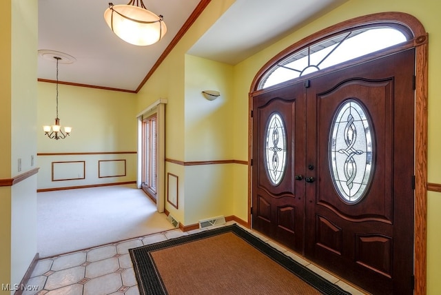 carpeted foyer featuring visible vents, baseboards, ornamental molding, and a chandelier