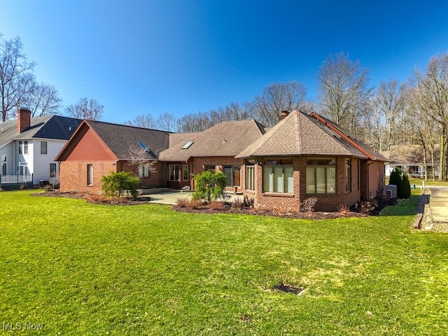 back of property featuring brick siding, a yard, and roof with shingles