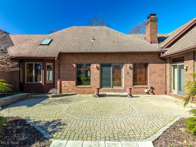 back of house featuring a chimney, a patio area, brick siding, and a shingled roof