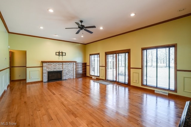 unfurnished living room featuring a brick fireplace, light wood-style floors, visible vents, and wainscoting