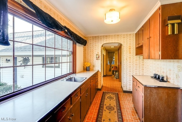 kitchen with wallpapered walls, crown molding, light countertops, arched walkways, and a sink