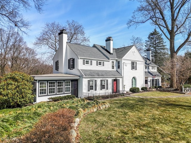 view of front of home featuring a chimney, a shingled roof, a front lawn, and a sunroom