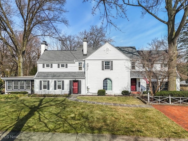 traditional-style home with a chimney, a front yard, and a sunroom