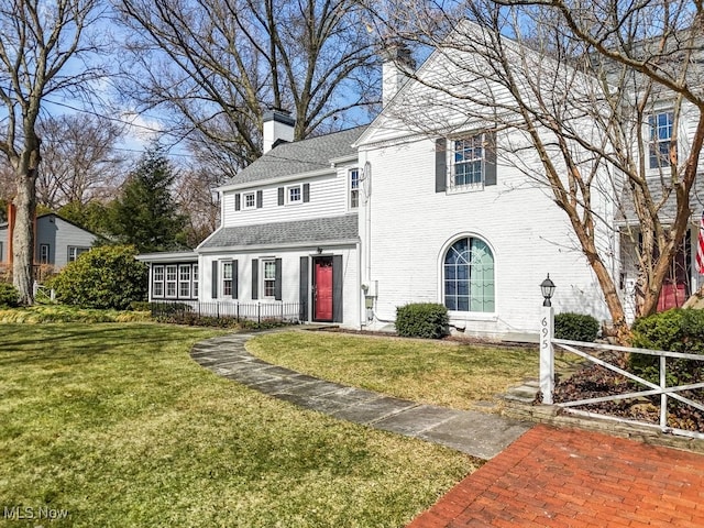 view of front of house featuring brick siding, a chimney, a front yard, and a shingled roof