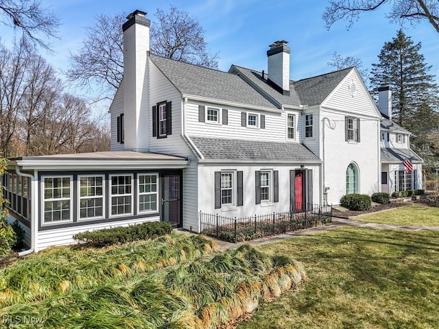 view of front facade featuring a shingled roof, a front lawn, a sunroom, and a chimney