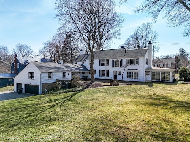 back of property with a sunroom, a yard, driveway, and a chimney