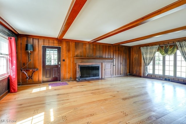 unfurnished living room with visible vents, beam ceiling, wood finished floors, wooden walls, and a fireplace