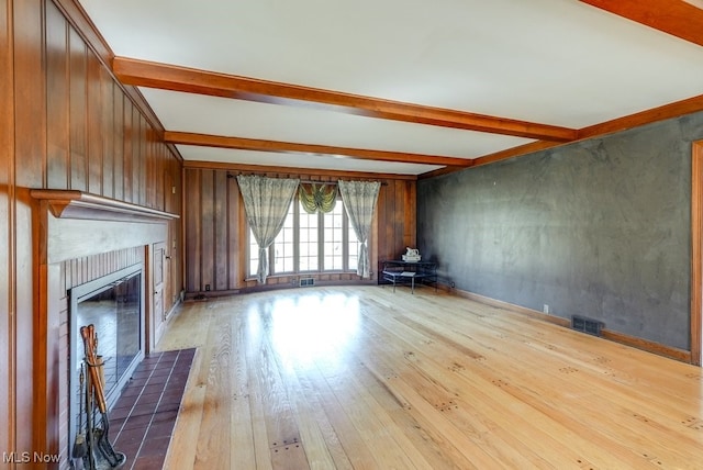 unfurnished living room with visible vents, beam ceiling, a glass covered fireplace, and hardwood / wood-style flooring