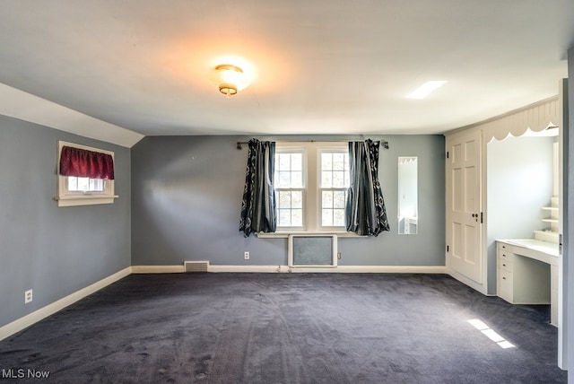 unfurnished bedroom with visible vents, baseboards, dark colored carpet, and lofted ceiling