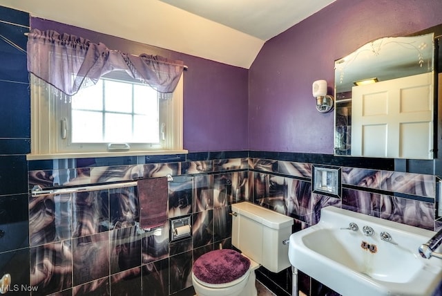 bathroom featuring toilet, a sink, tile walls, wainscoting, and lofted ceiling