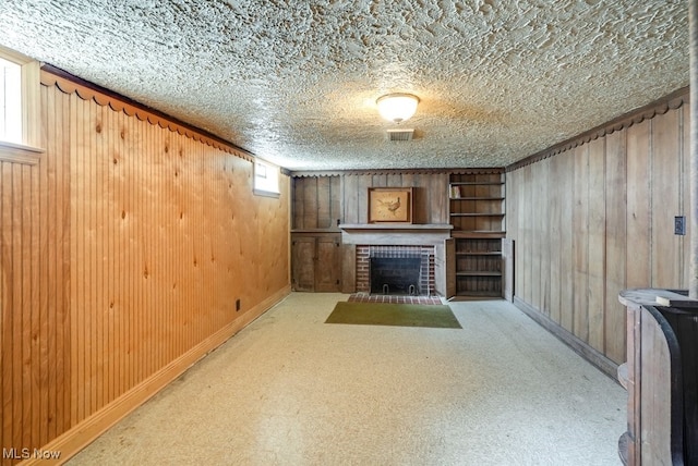 unfurnished living room with a brick fireplace, wooden walls, carpet, and a textured ceiling