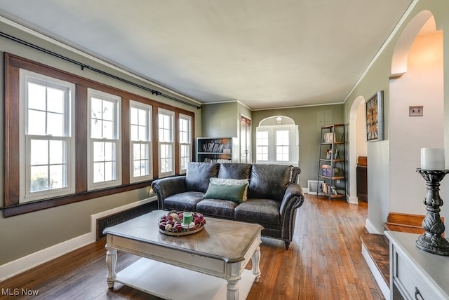 living area with baseboards, arched walkways, radiator, and wood finished floors