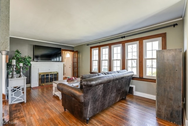 living area featuring visible vents, baseboards, a fireplace, wood-type flooring, and crown molding