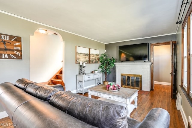 living area featuring stairway, wood finished floors, a fireplace, arched walkways, and ornamental molding