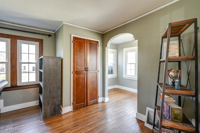 interior space featuring hardwood / wood-style floors, baseboards, arched walkways, and ornamental molding